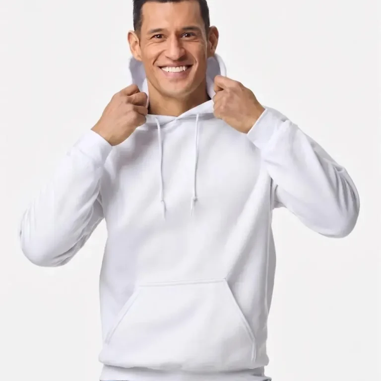 Man in a white hooded sweatshirt and blue jeans smiles while holding hoodie strings