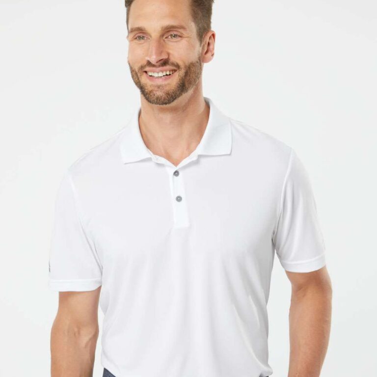 Man in white Adidas golf polo and navy belt smiling against white background