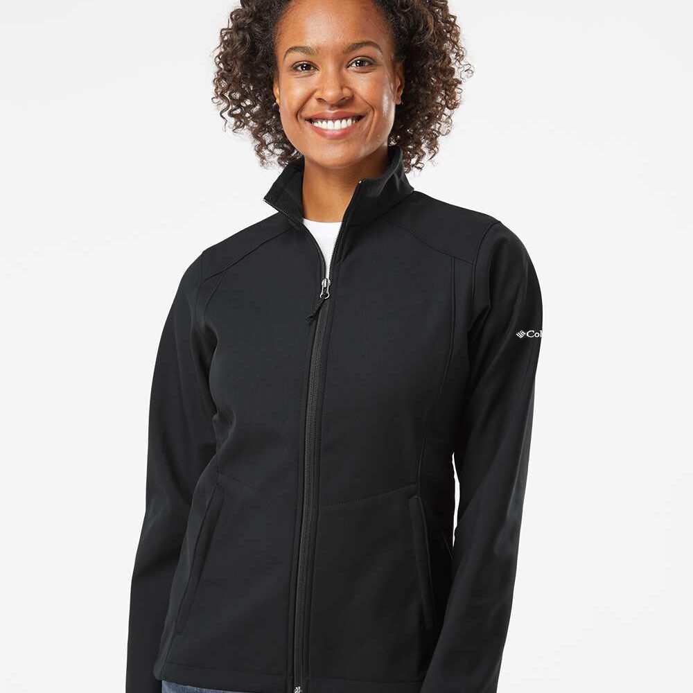 Woman wearing a black Columbia softshell jacket and blue jeans smiling.