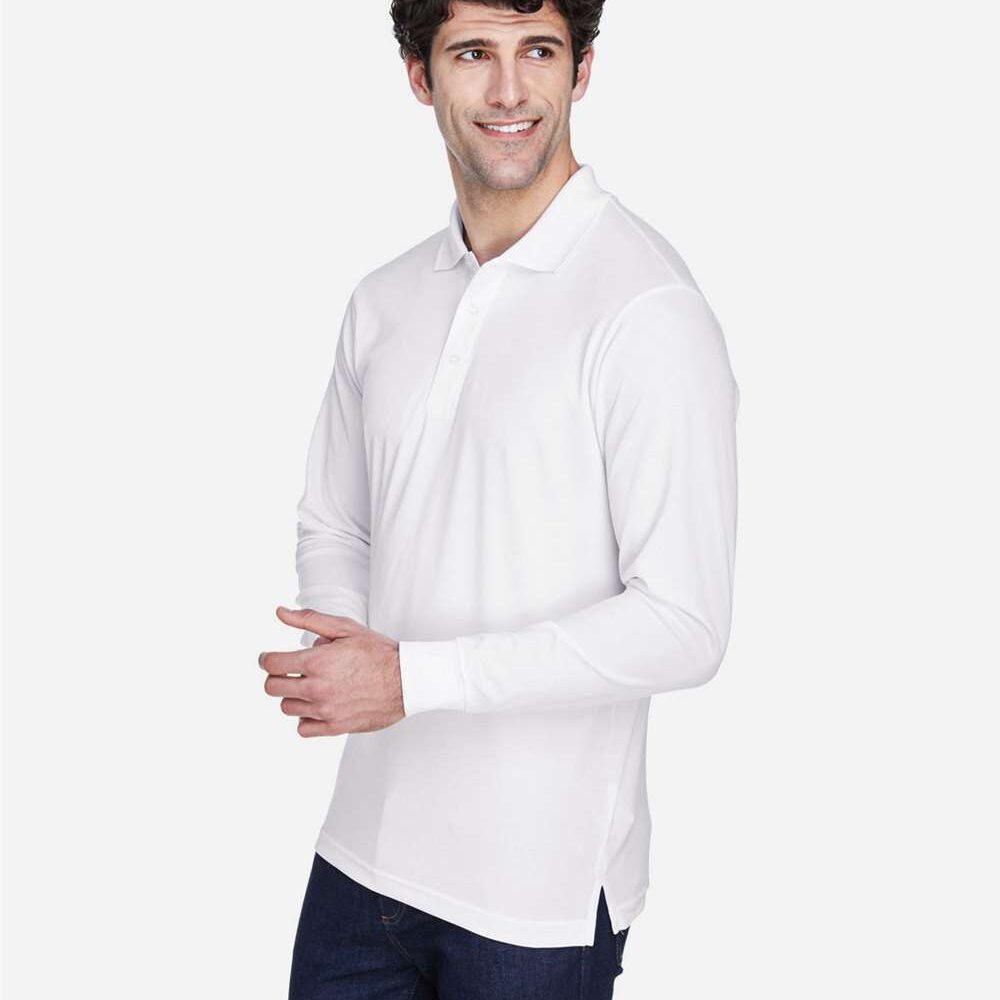 Man in white long sleeve polo shirt and dark jeans smiles, looking to the side.