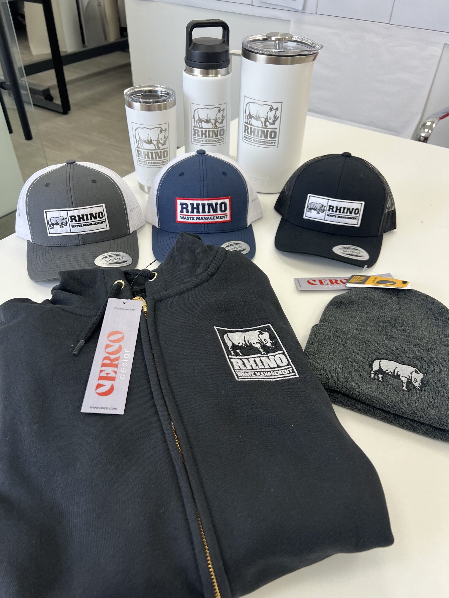 Rhino Waste Management branded merchandise including hats, jackets, tumblers, and a toque.